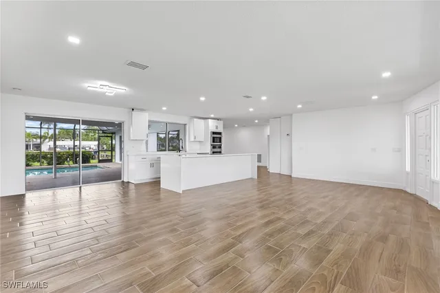 a view of an empty room with wooden floor and a kitchen