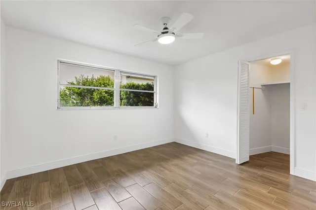 an empty room with wooden floor ceiling fan and windows