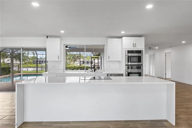 a large white kitchen with kitchen island a large window appliances and cabinets