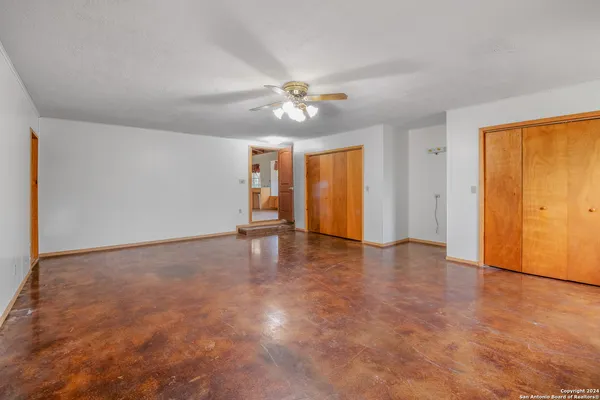an empty room with chandelier fan and windows