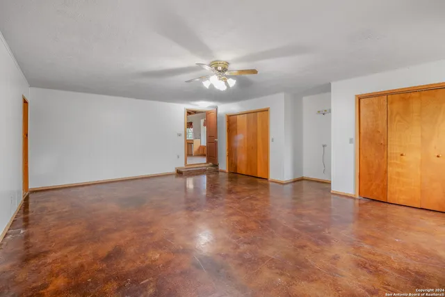 an empty room with chandelier fan and windows