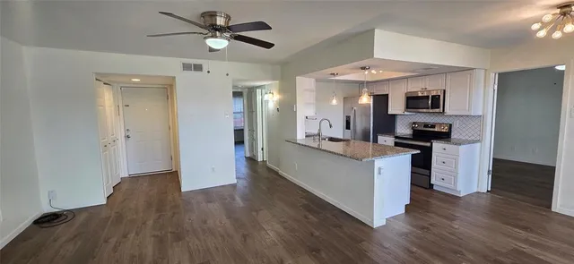 a living room with stainless steel appliances kitchen island hardwood floor and a ceiling fan