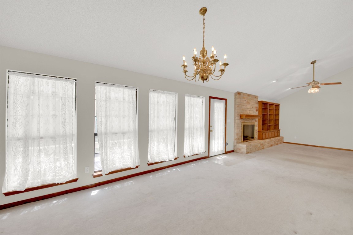 1403 Stone Ridge Drive Taylor, TX 76574 - Photo 16 of 39 Unfurnished living room featuring vaulted ceiling, a chandelier, carpet flooring, a fireplace, and a ceiling fan