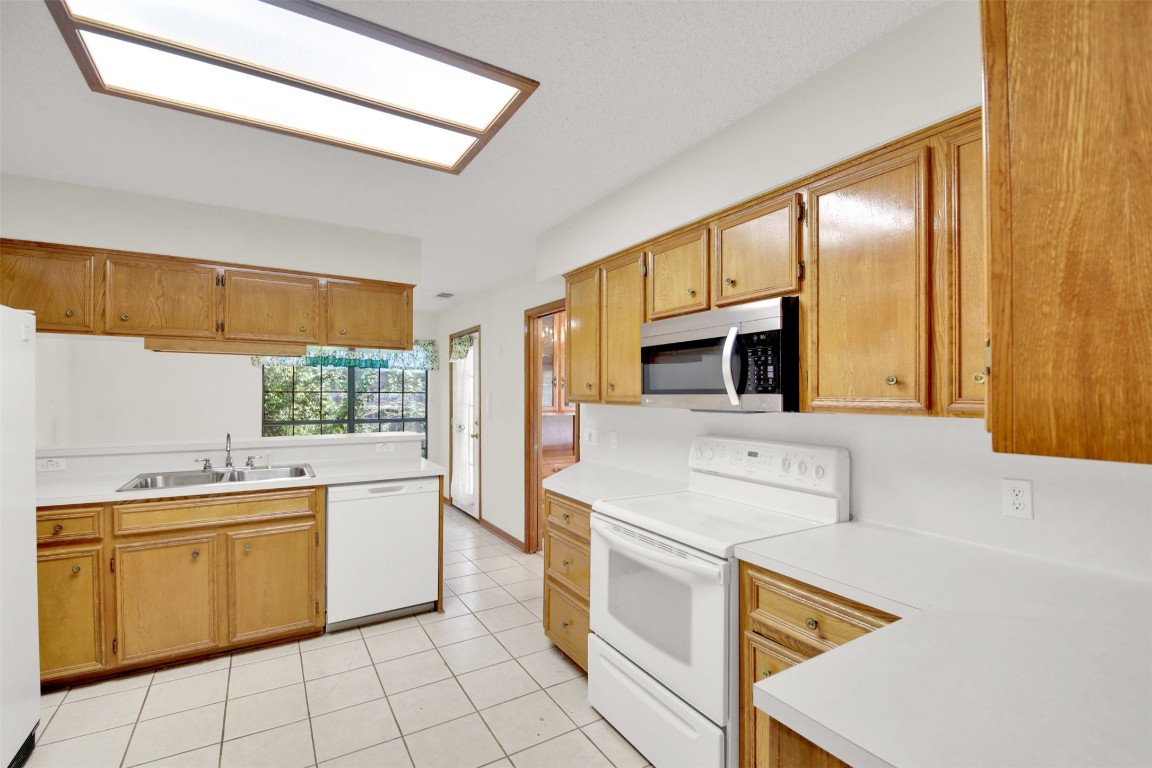1403 Stone Ridge Drive Taylor, TX 76574 - Photo 17 of 39 Kitchen with white appliances, light countertops, light tile patterned flooring, a skylight, and brown cabinets