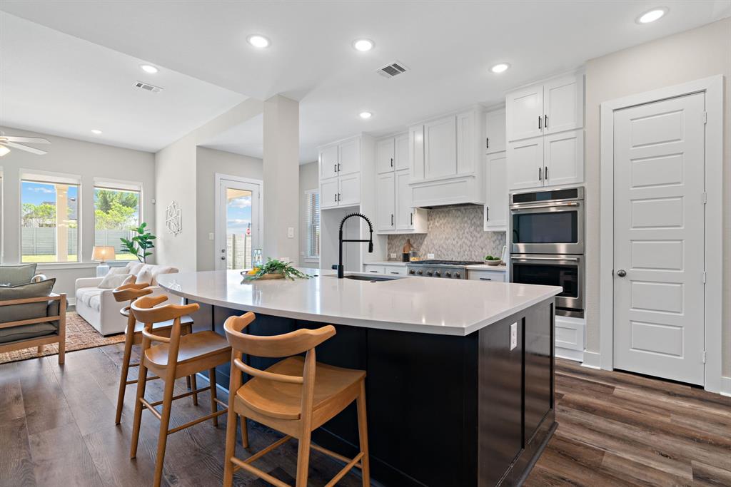 1821 Stonewall Road Argyle, TX 76226 - Photo 5 of 40 Open-concept kitchen featuring a dark-toned island with light countertops, white cabinetry, stainless steel double ovens, and wood-finish flooring