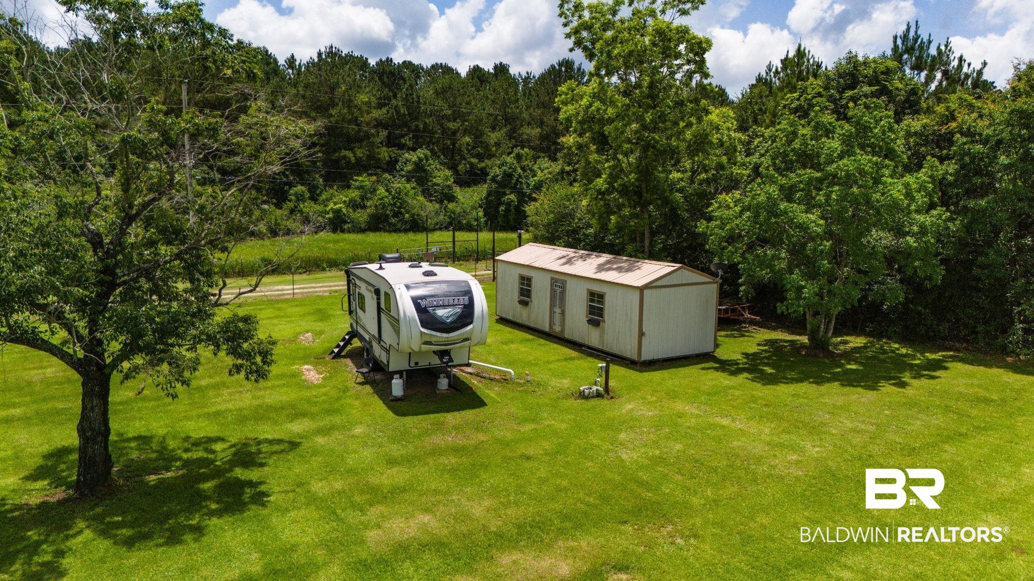 34985b Spring Road South, Unit B Stapleton, AL 36578 - Photo 6 of 31 Expansive green lawn featuring a storage shed with multiple windows, a mature tree, and a forested backdrop