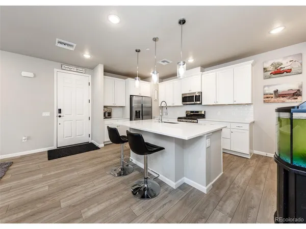 a kitchen with stainless steel appliances kitchen island granite countertop a refrigerator a stove and white cabinets with wooden floor