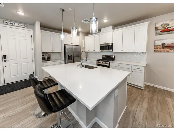 a kitchen with stainless steel appliances kitchen island granite countertop a refrigerator a stove and white cabinets with wooden floor