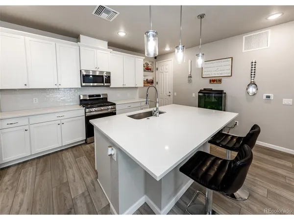 a kitchen with stainless steel appliances kitchen island granite countertop a stove a sink a refrigerator and white cabinets with wooden floor