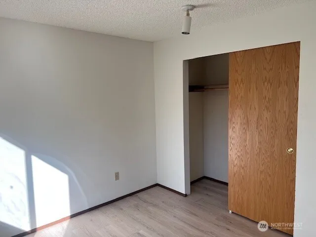 a view of an empty room with wooden floor and closet