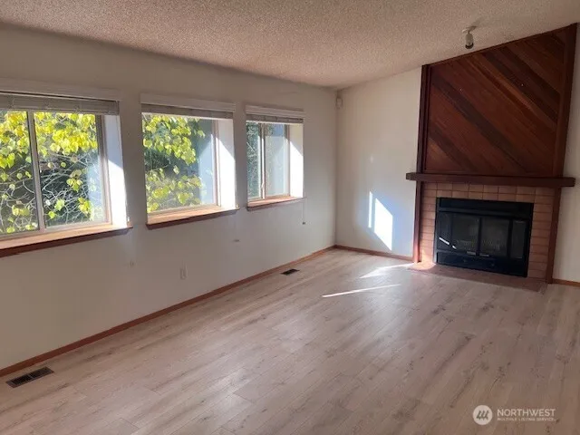 an empty room with wooden floor fireplace and windows