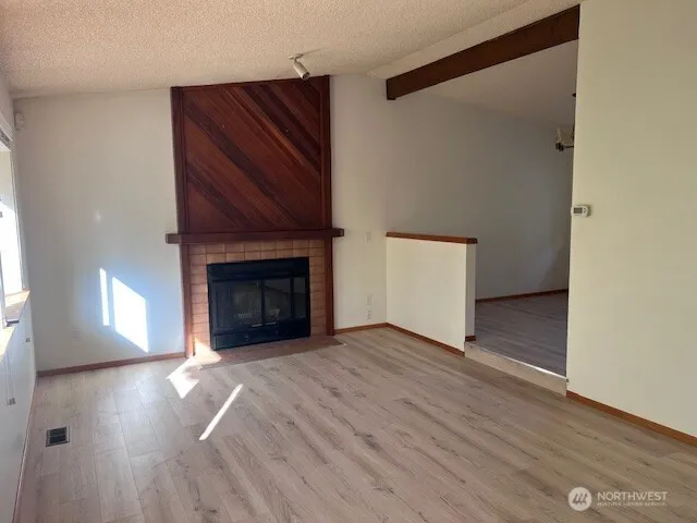 a view of an empty room with wooden floor and a fireplace