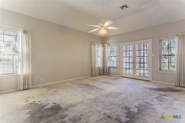 an empty room with chandelier fan and windows