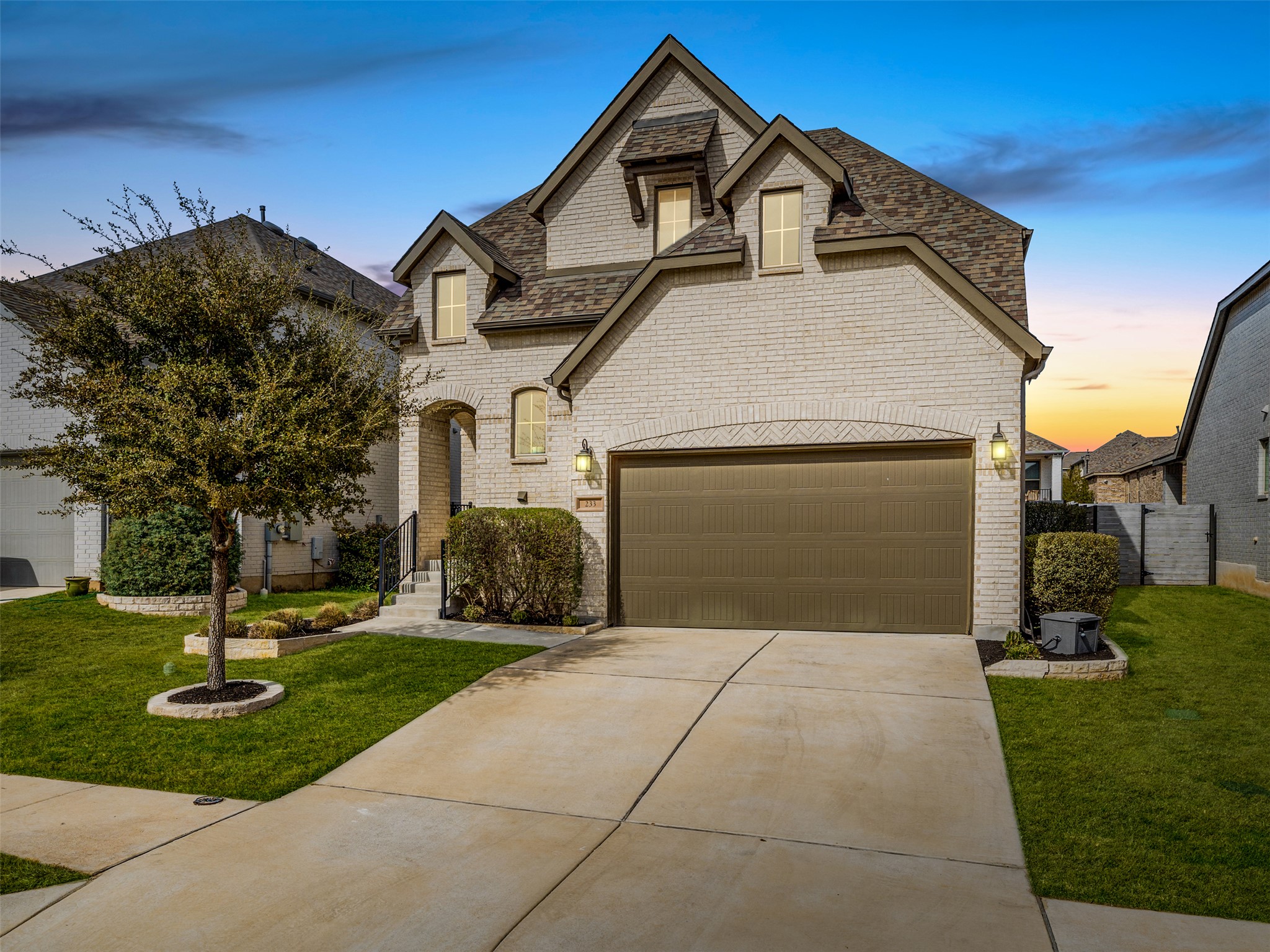 French country inspired facade with concrete driveway, a front lawn, brick siding, a shingled roof, and a garage