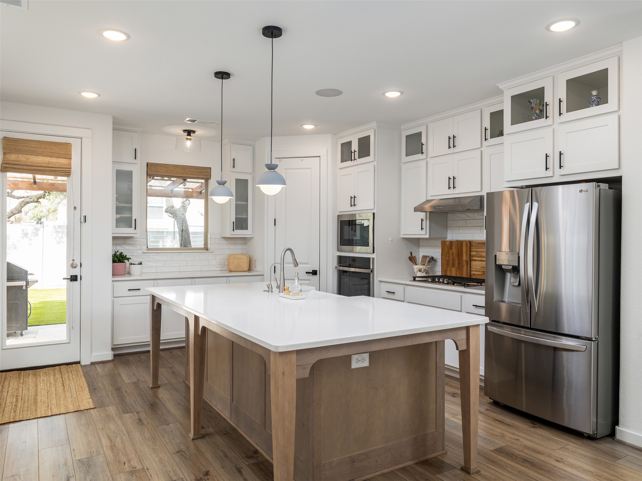 233 Arrowhead Mound Road Georgetown, TX 78628 - Photo 3 of 40 Kitchen featuring glass insert cabinets, stainless steel appliances, backsplash, a kitchen island with sink, and two tone cabinetry