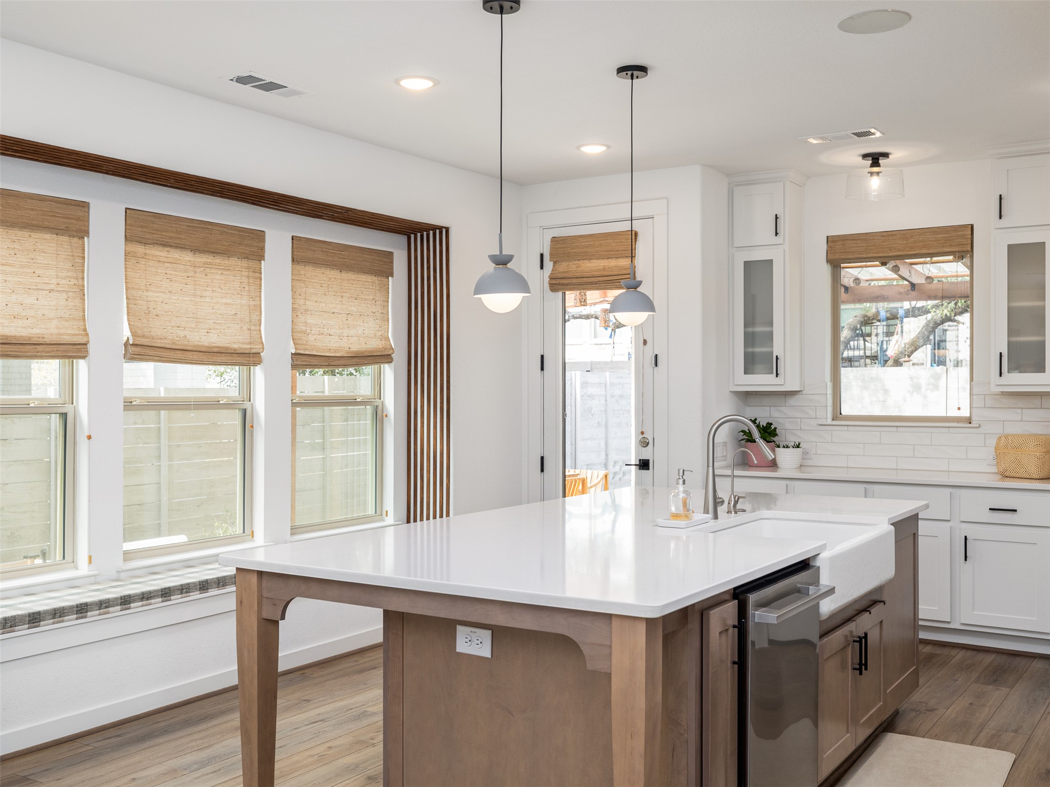 233 Arrowhead Mound Road Georgetown, TX 78628 - Photo 7 of 40 Dual tone kitchen featuring decorative backsplash, decorative light fixtures, glass fronted cabinets, a kitchen island with sink, and healthy amount of natural light