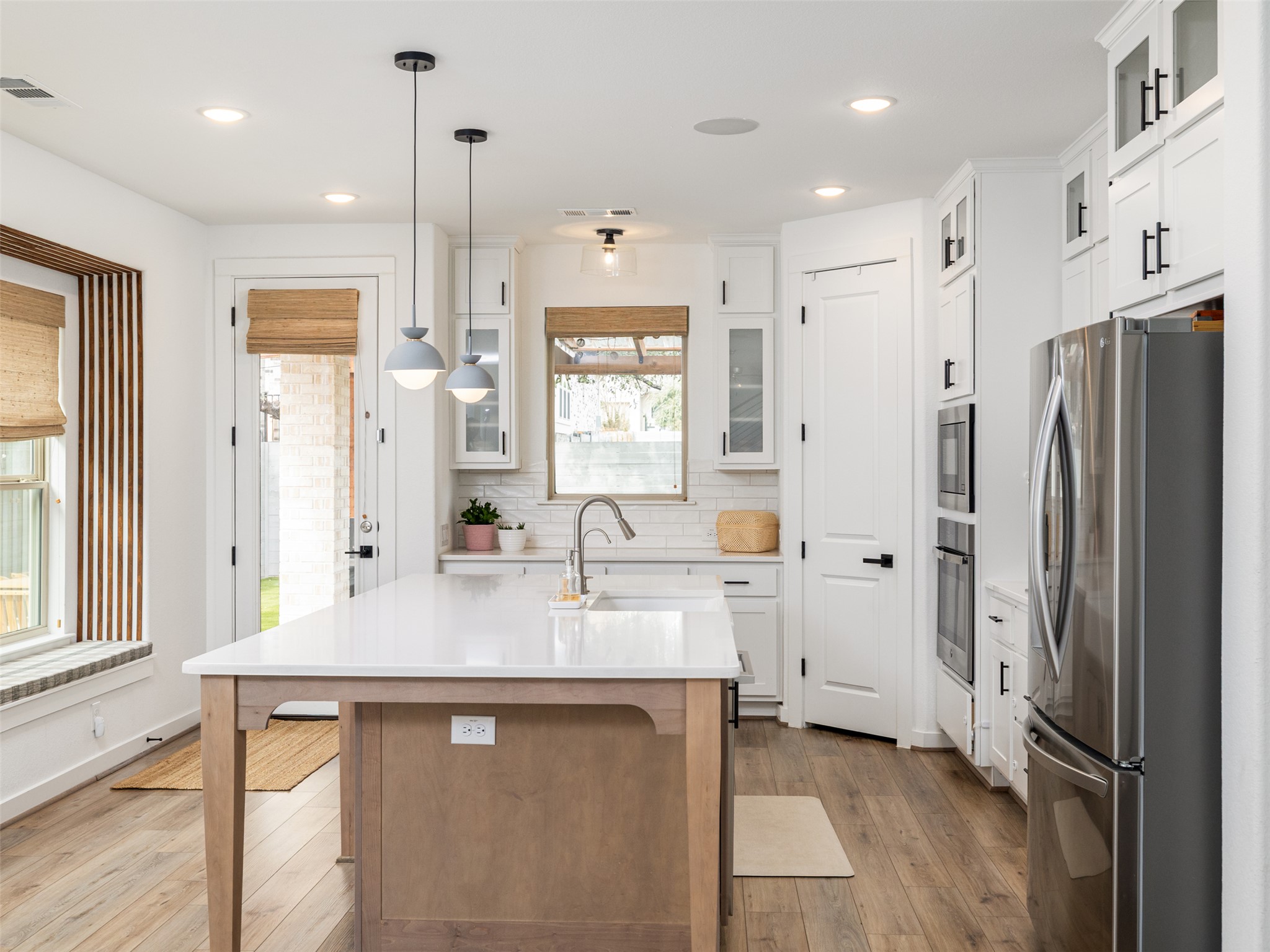 233 Arrowhead Mound Road Georgetown, TX 78628 - Photo 8 of 40 Dual tone kitchen with glass insert cabinets, stainless steel appliances, a center island with sink, light wood-style flooring, and hanging light fixtures