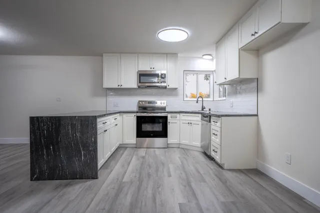 a kitchen with granite countertop wooden floors stainless steel appliances and sink