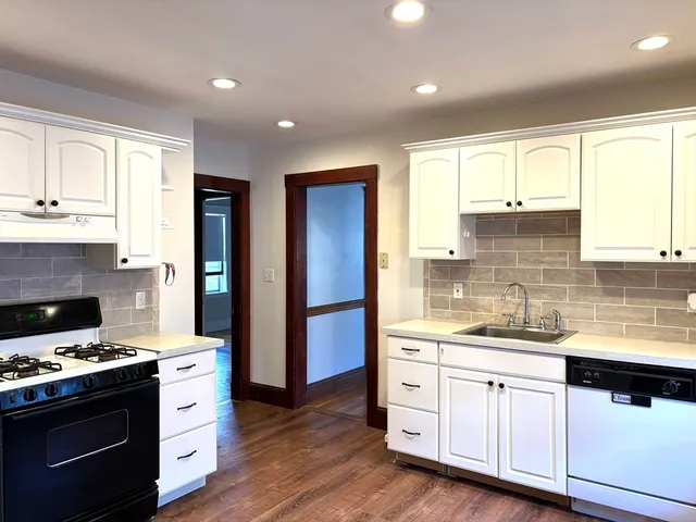 a kitchen with stainless steel appliances white cabinets a sink and a wooden floor