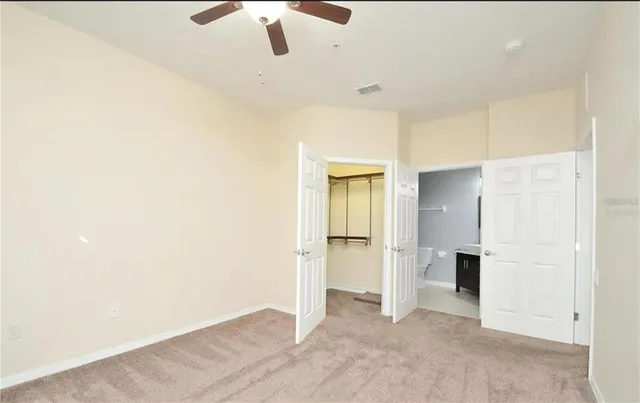 an empty room with chandelier fan and kitchen view