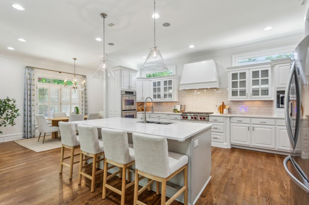 a kitchen with stainless steel appliances granite countertop a stove top oven a sink dishwasher a dining table and chairs with wooden floor