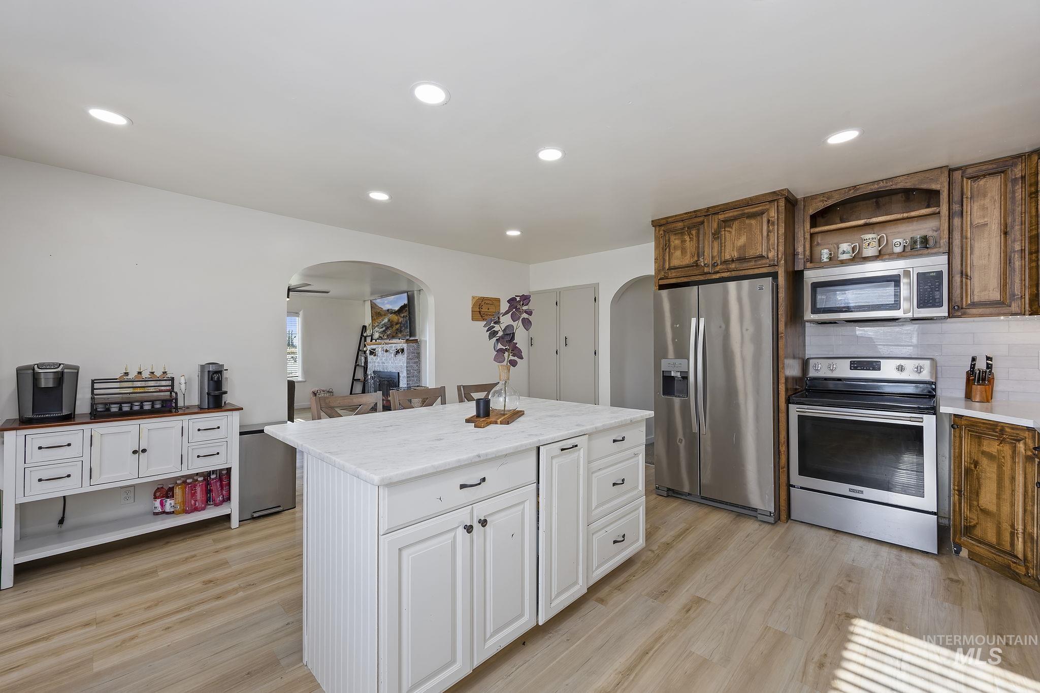 128 South 100 East Rupert, ID 83350 - Photo 14 of 44 Kitchen featuring appliances with stainless steel finishes, arched walkways, light wood-style floors, a kitchen island, and open shelves