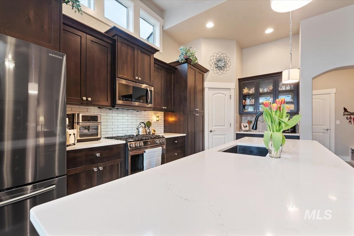 1447 West Arch Rock Street Meridian, ID 83646 - Photo 14 of 43 Kitchen featuring stainless steel appliances, glass fronted cabinets, dark wood finish cabinetry, arched walkways, and decorative backsplash