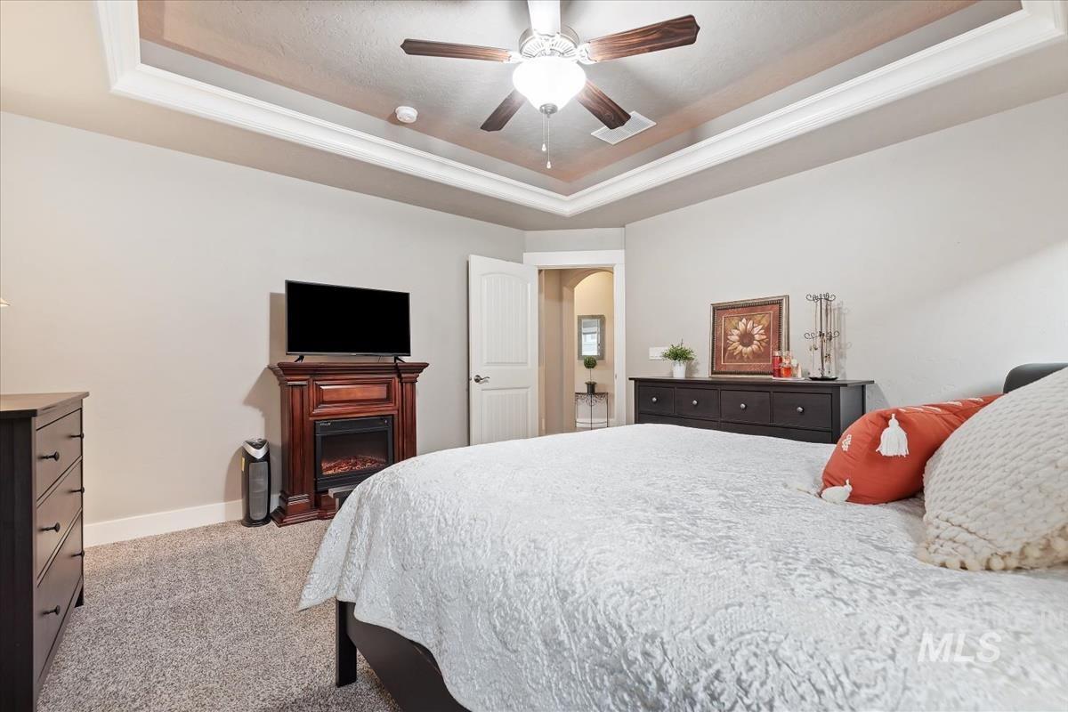 1447 West Arch Rock Street Meridian, ID 83646 - Photo 19 of 43 Bedroom with a raised ceiling, light carpet, a glass covered fireplace, and a ceiling fan