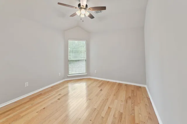 an empty room with wooden floor fan and windows