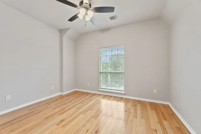 an empty room with wooden floor fan and windows