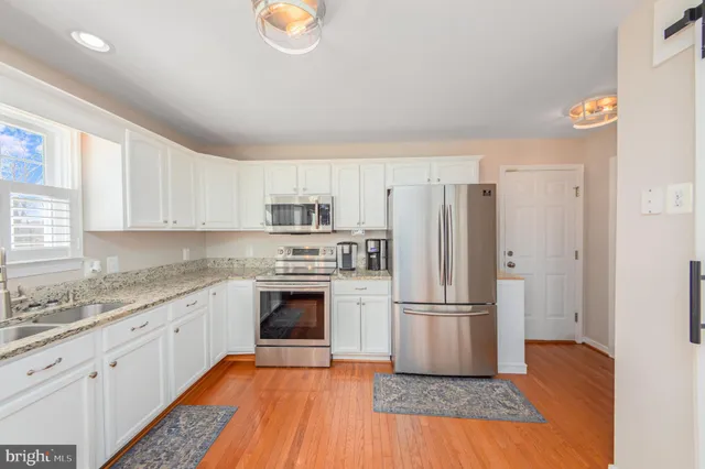 a kitchen with granite countertop a refrigerator oven a sink and wooden floors