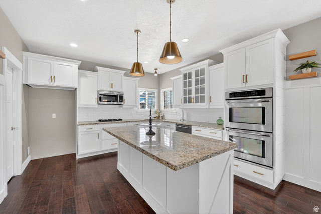 14714 South Bright Wood Road Herriman, UT 84096 - Photo 13 of 41 Kitchen featuring appliances with stainless steel finishes, granite/stone countertops, white cabinets, glass insert cabinets, and pendant lighting