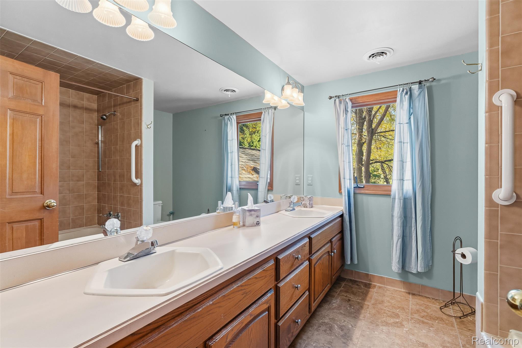 8135 Ranch Estates Road Clarkston, MI 48348 - Photo 33 of 53 Double vanity with integrated sinks, wood-finish cabinetry, full-width mirror, and tiled shower surround