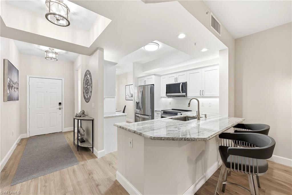 401 Bayfront Place, Unit 3307 Naples, FL 34102 - Photo 6 of 28 Kitchen featuring white cabinets, light stone counters, a peninsula, stainless steel appliances, and a kitchen bar
