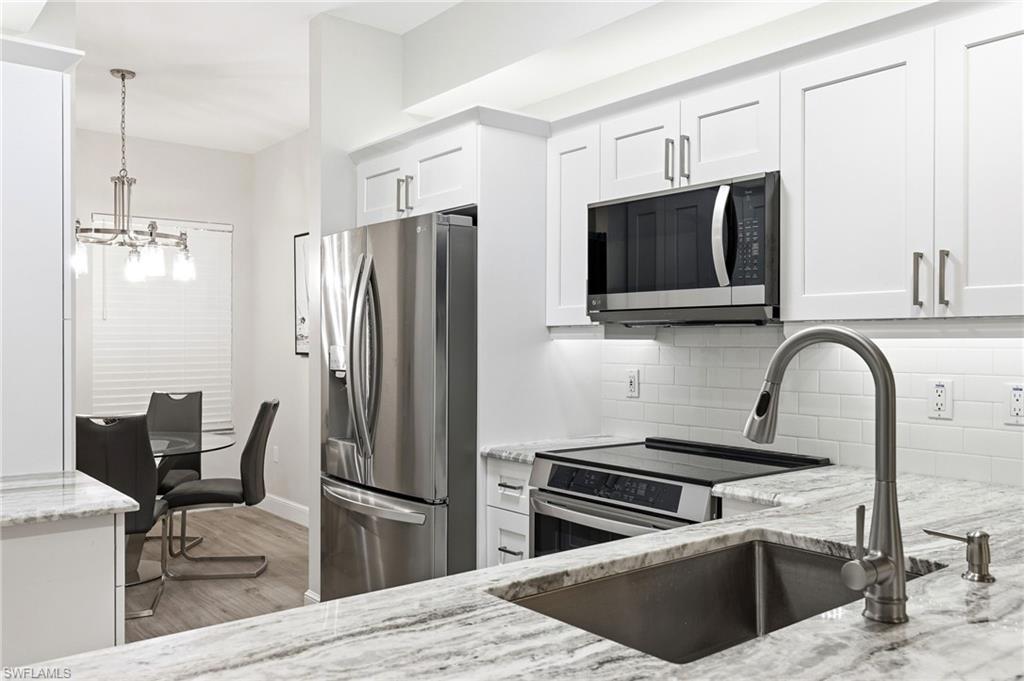 401 Bayfront Place, Unit 3307 Naples, FL 34102 - Photo 8 of 28 Kitchen with appliances with stainless steel finishes, light stone counters, white cabinets, decorative light fixtures, and a chandelier