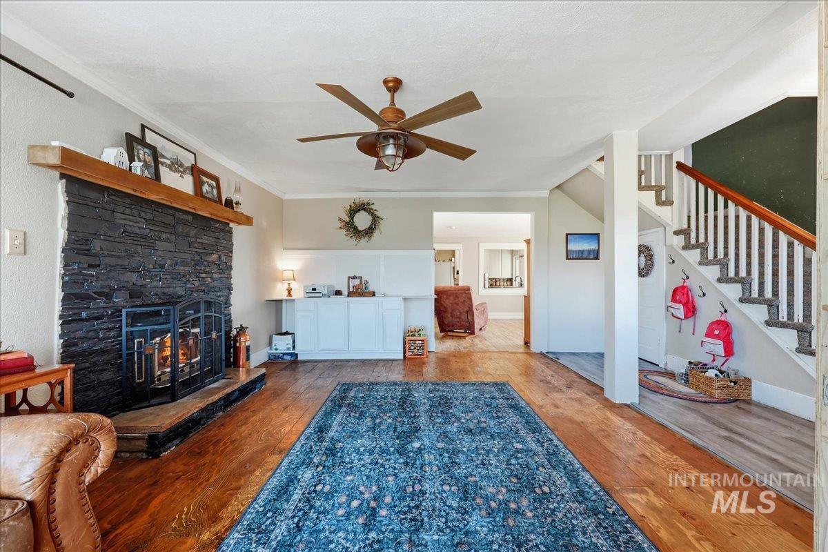 148 Glascock Road Weiser, ID 83672 - Photo 14 of 32 Living area featuring wood finished floors, a ceiling fan, a stone fireplace, and crown molding