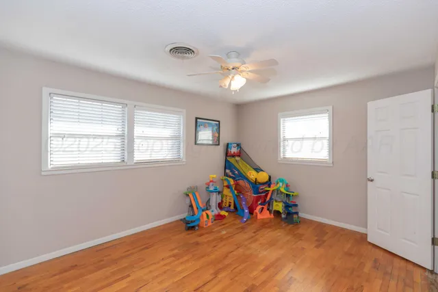 a view of a room with wooden floor ceiling fan and windows