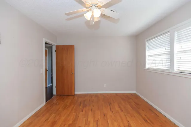 an empty room with wooden floor chandelier fan and windows