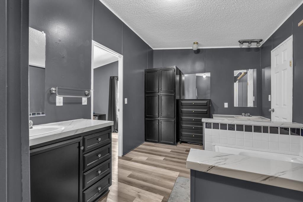 3615 Spring Valley Road Lorena, TX 76655 - Photo 20 of 33 Bathroom featuring dual vanity areas with dark cabinetry and light countertops, wood-finish flooring, and a tiled tub surround