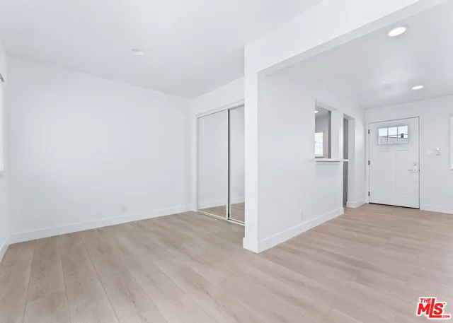 an empty room with wooden floor and a kitchen