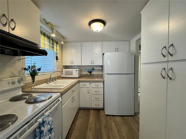 a kitchen with sink a refrigerator and white cabinets with wooden floor