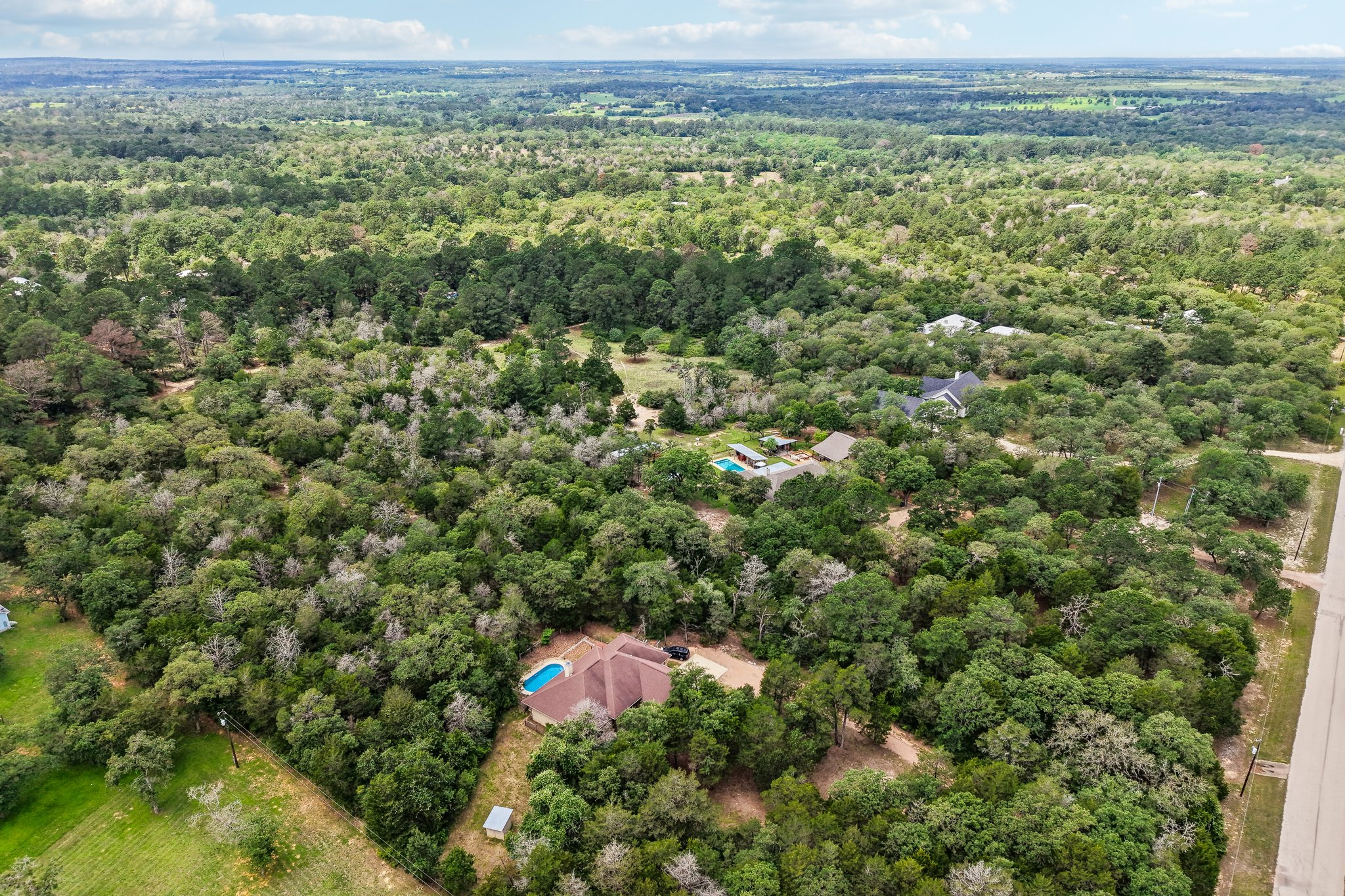 267 Corral Road Smithville, TX 78957 - Photo 39 of 40 Expansive treed acreage featuring a single-story residence with a brown roof and an adjacent inground swimming pool