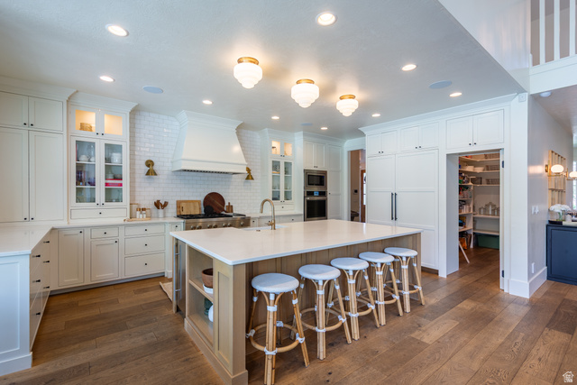 630 East Center Street Alpine, UT 84004 - Photo 17 of 115 Gourmet kitchen featuring a large central island with a light-toned wood-finish base, ample white cabinetry, a built-in range hood above a professional-style range, light-colored countertops, and wood-finish flooring