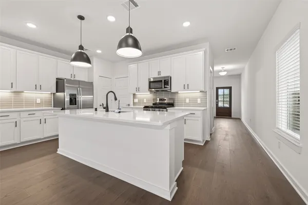 a kitchen with stainless steel appliances a refrigerator a sink dishwasher a oven with white cabinets and wooden floor