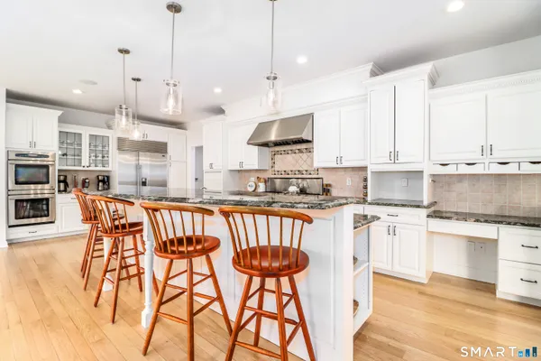 a kitchen with stainless steel appliances granite countertop a stove a sink a center island a refrigerator and a wooden floor