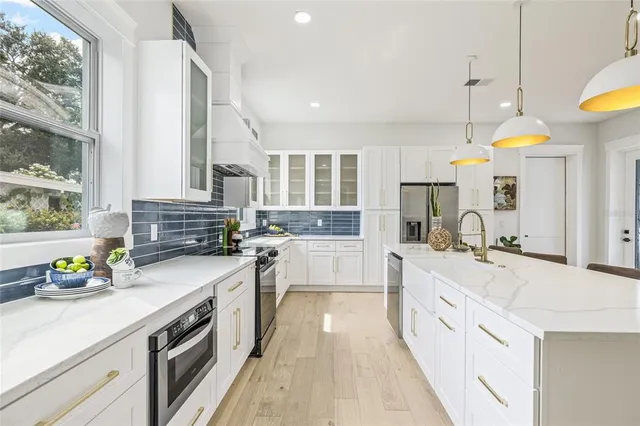 a large white kitchen with stainless steel appliances granite countertop a stove a sink and a refrigerator