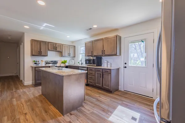 a kitchen with stainless steel appliances granite countertop a stove top oven a sink dishwasher and a refrigerator with wooden floor