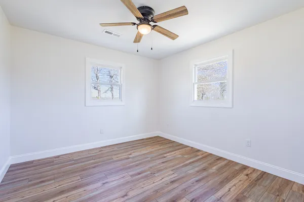 an empty room with wooden floor fan and windows