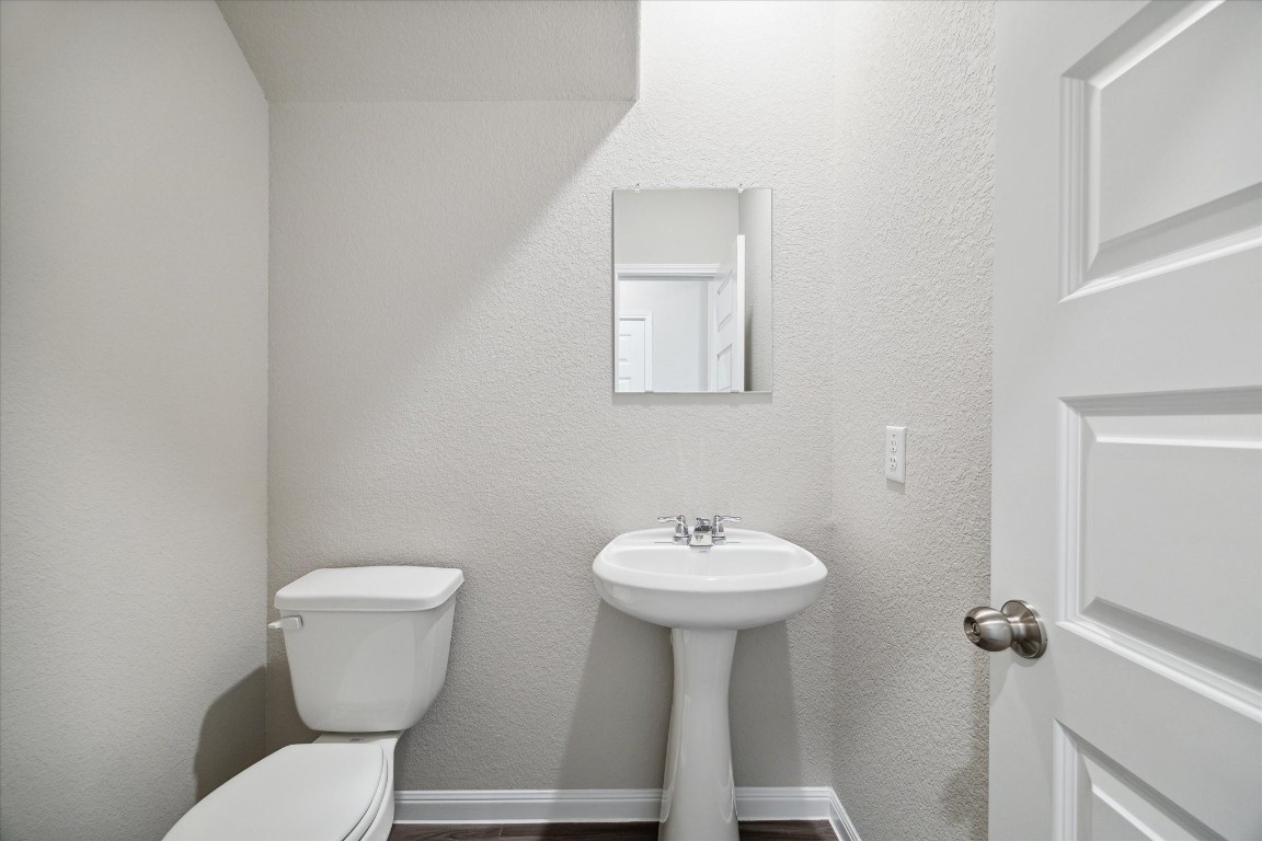 715 Gavin Walker Drive Rosharon, TX 77583 - Photo 14 of 15 This is a compact, modern half-bathroom featuring a pedestal sink, a toilet, and a small mirror. The space is bright with neutral-colored walls and has a clean, minimalistic design.
