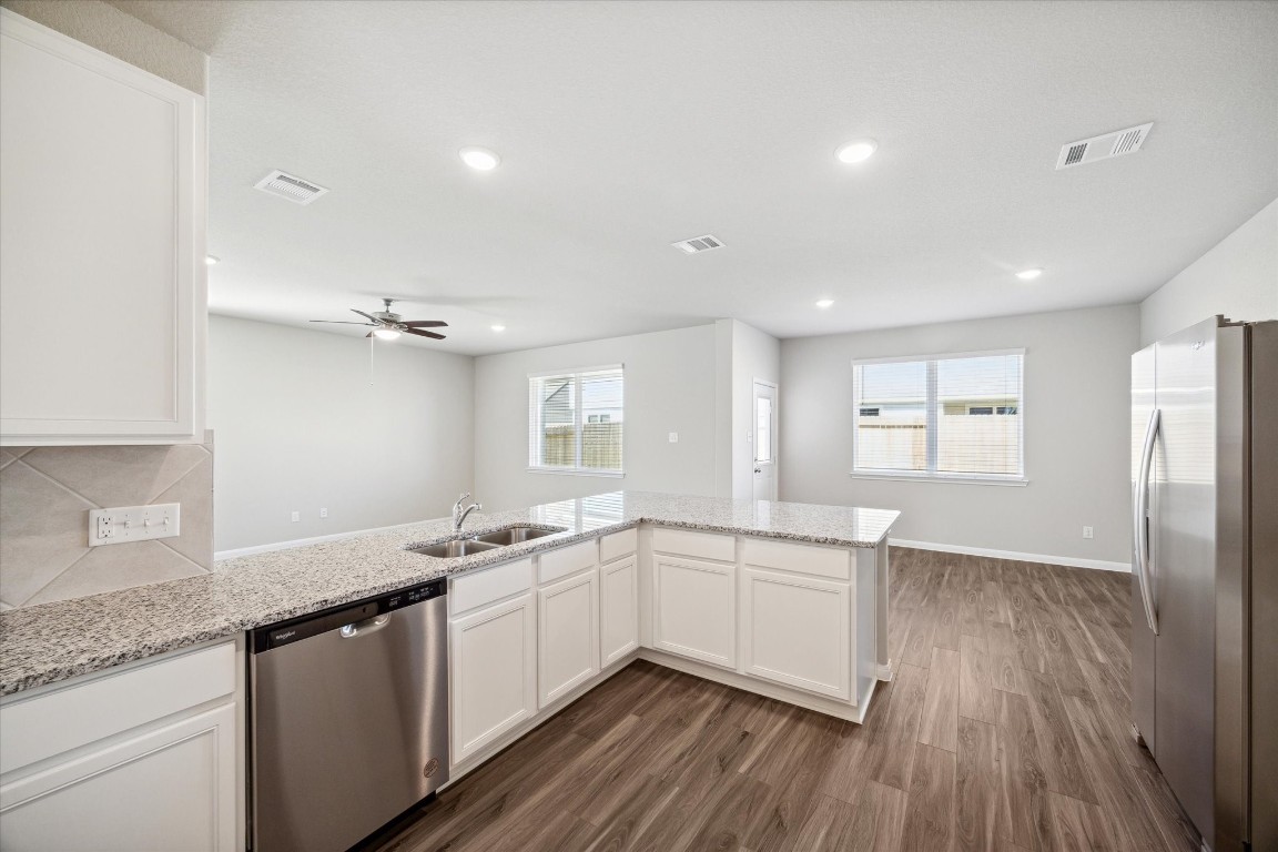 715 Gavin Walker Drive Rosharon, TX 77583 - Photo 3 of 15 This photo showcases a modern open-concept kitchen and living area with sleek granite countertops, stainless steel appliances, and wood-style flooring. The space is bright and airy, featuring ample natural light and recessed lighting, creating a welcoming environment.